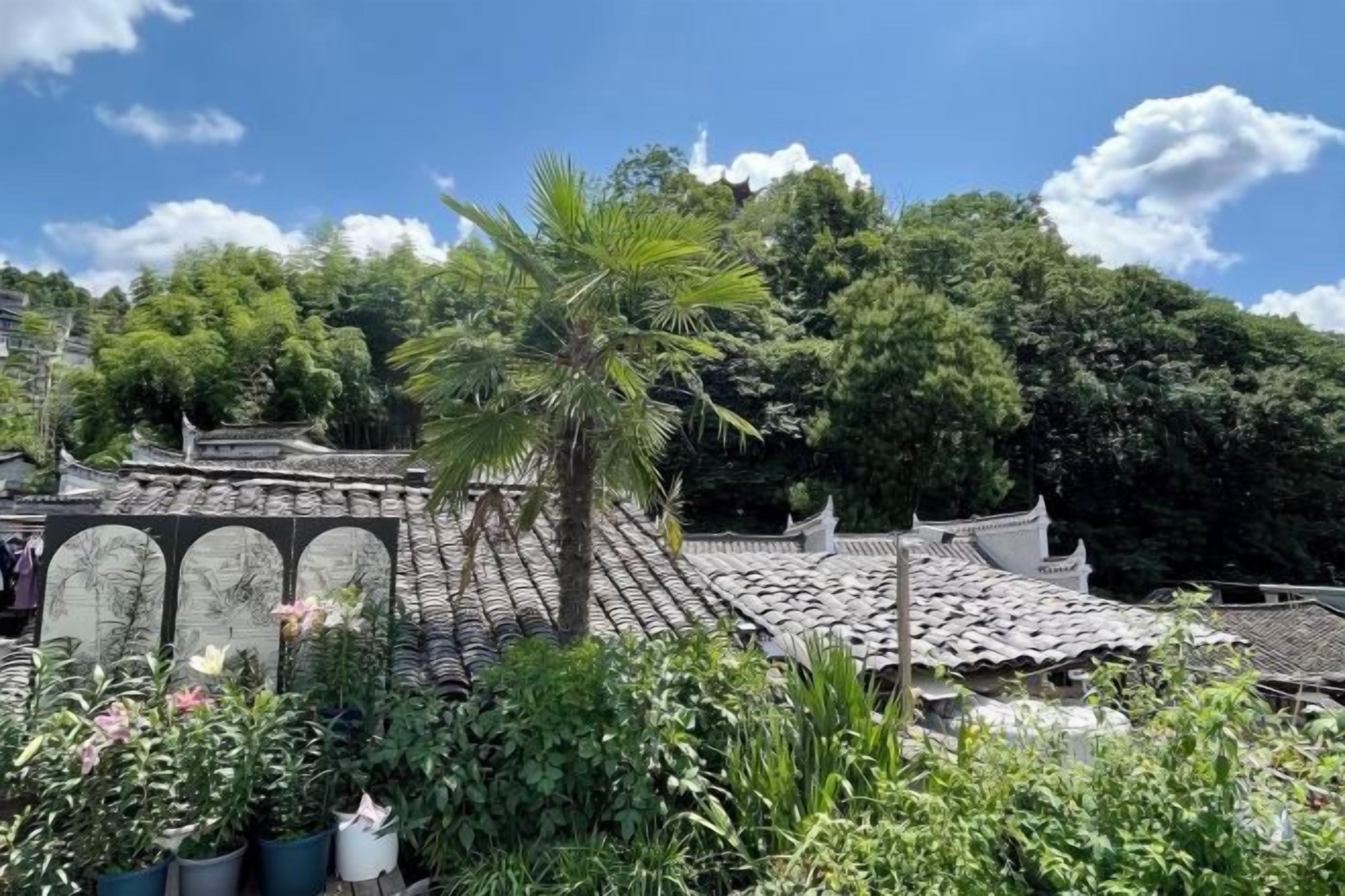 A traditional building with a tiled roof, surrounded by lush greenery and a clear sky.