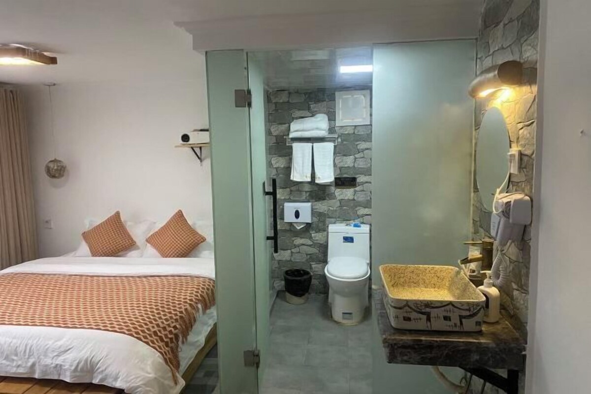 Una habitación de hotel con cama, baño con pared de piedra y lavabo con recipiente decorativo.