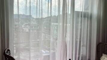A room with a view through sheer curtains, a wicker chair, and a small table.