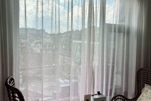 A room with a view through sheer curtains, a wicker chair, and a small table. - Phoenix Moonlight View Inn (Fenghuang County)