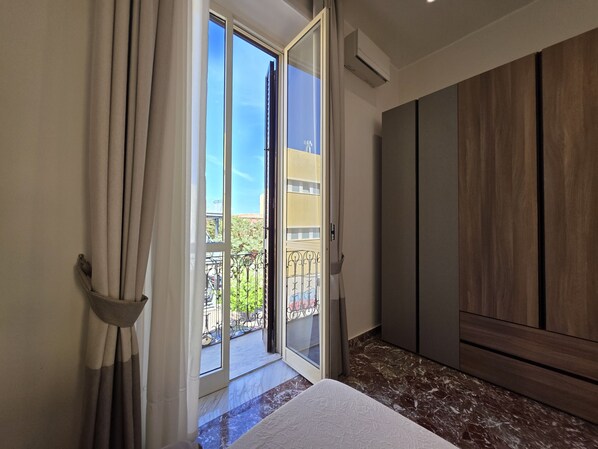 A room with a sliding glass door leading to a balcony, a bed with a white bedspread, and a wooden wardrobe.