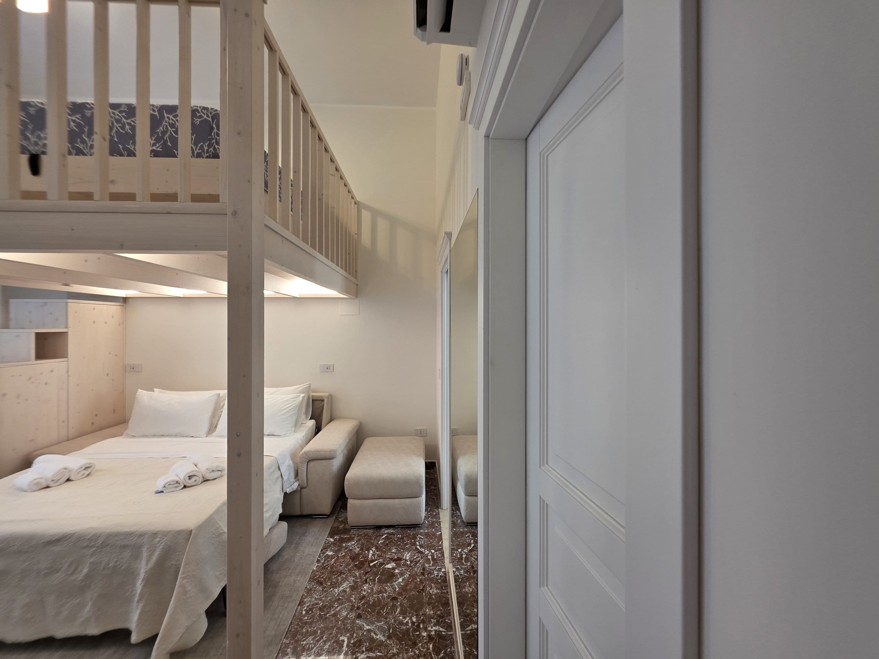 Quarto de hotel com beliche, sofá, uma mesa pequena e uma porta.