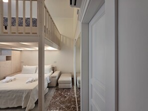 A hotel room with a bunk bed, a sofa, a small table, and a door.