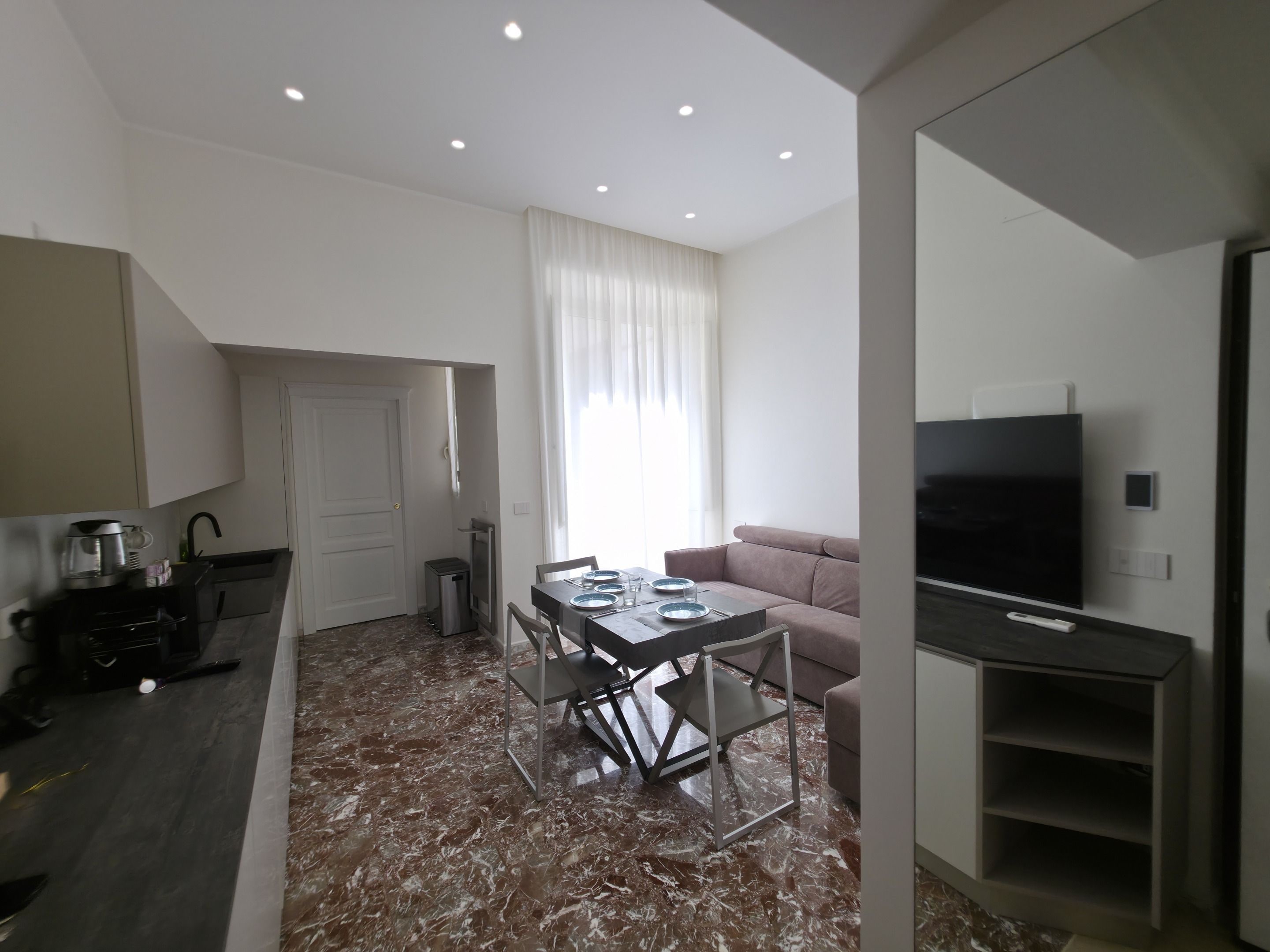 Espaço moderno com área de jantar, sofá, TV e cozinha.