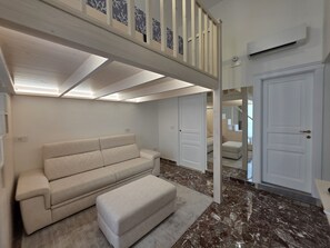 A room with a sofa, ottoman, and a ceiling with a skylight.