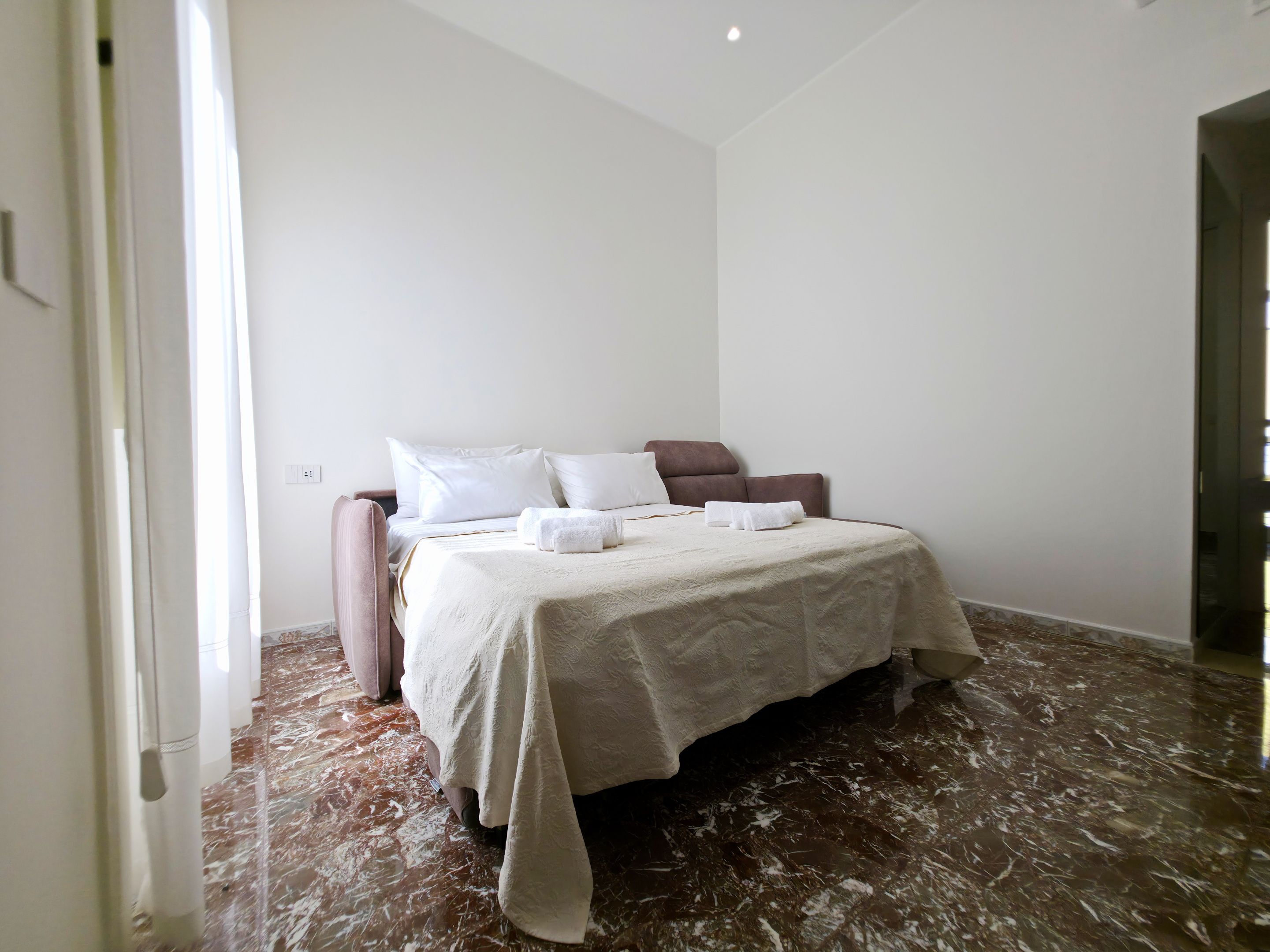 A bedroom with a bed, pillows, a bedside table, and a marble floor.