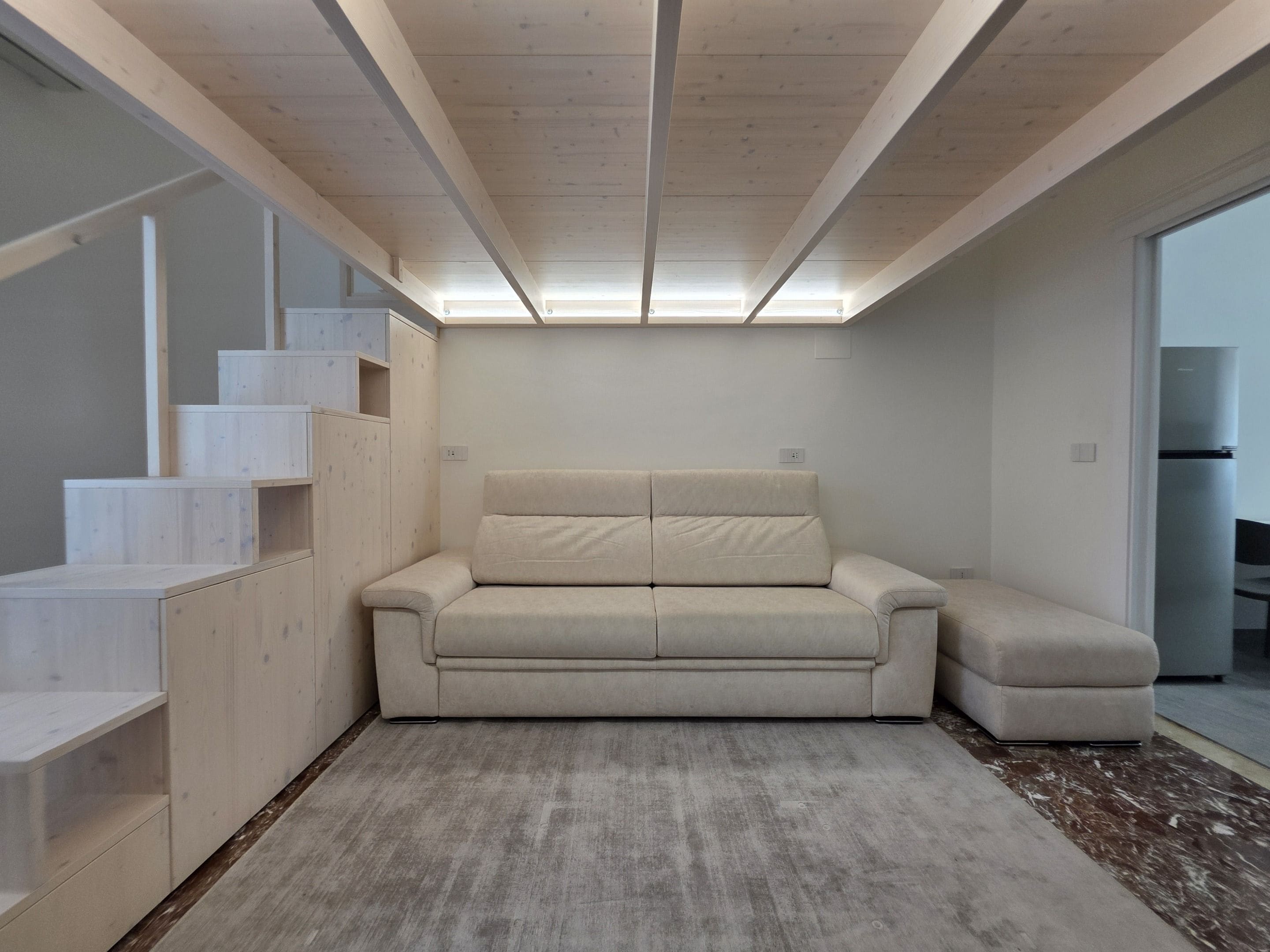 A modern interior with a sofa, built-in shelving, and a large window.
