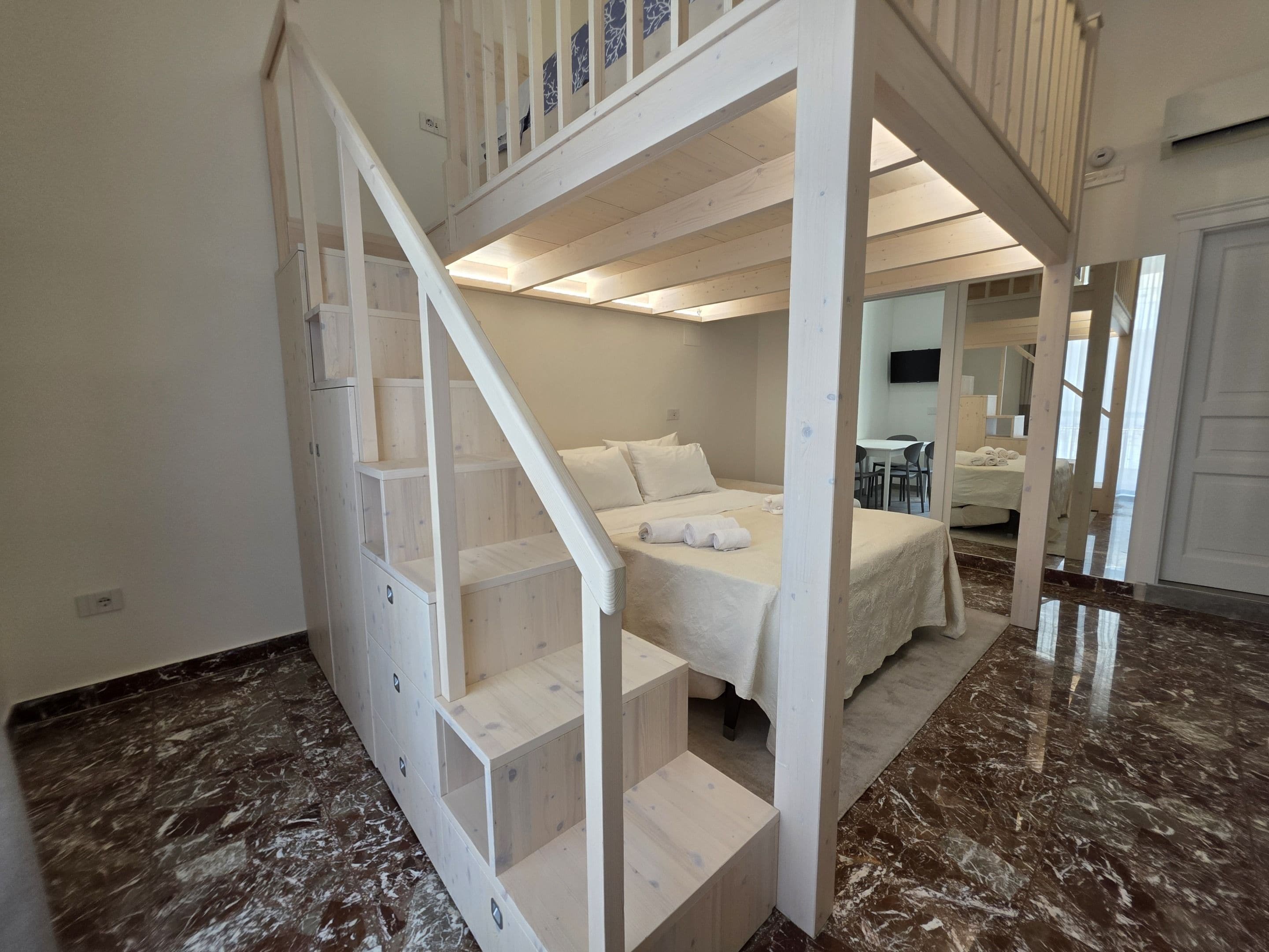 A bedroom with a bunk bed, a wooden staircase, and a bathroom visible in the background.