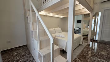 A bedroom with a bunk bed, a wooden staircase, and a bathroom visible in the background.