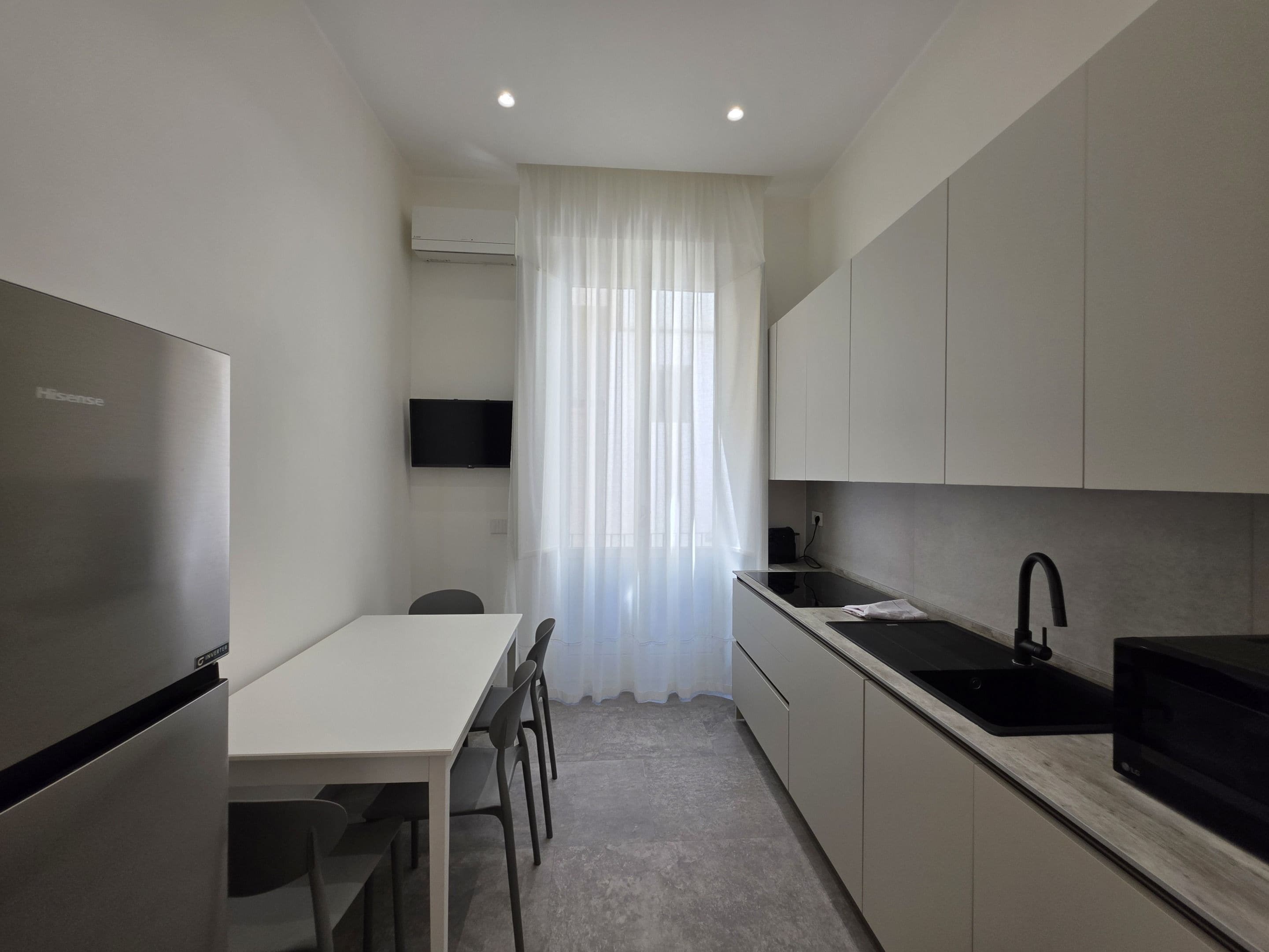 A compact kitchen with a refrigerator, a microwave, a sink, and a dining area with chairs.