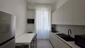 A compact kitchen with a refrigerator, a microwave, a sink, and a dining area with chairs.