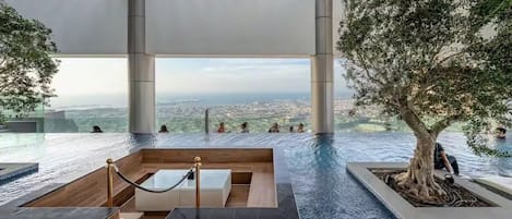 A rooftop infinity pool with a view of the city, surrounded by trees and modern architecture.