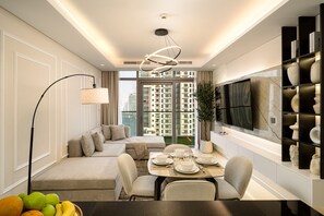 A modern living room with a sofa, dining table, and a large TV mounted on the wall. - Gogoto11 2BR Premium Infinity Pool & Burj View (Dubai)