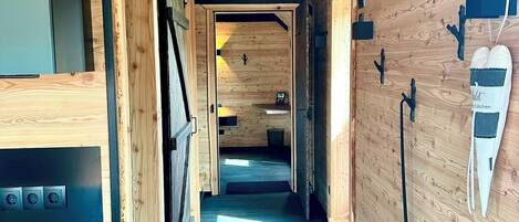 Un pasillo estrecho con paredes de madera y suelo oscuro, que lleva a una habitación con una puerta al final.