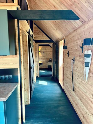 Un pasillo estrecho con paredes de madera y suelo oscuro, que lleva a una habitación con una puerta al final.