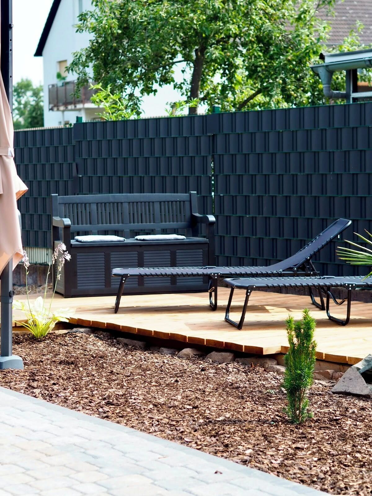 A patio area with a bench, a lounge chair, and a small plant.