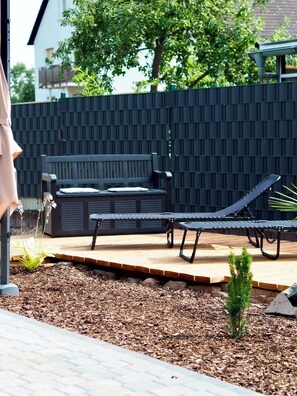 A patio area with a bench, a lounge chair, and a small plant.