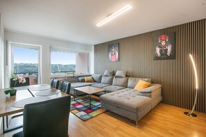 A modern living room with a sectional sofa, a dining table, and a view of the outdoors.