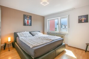 A bedroom with a bed, a bedside lamp, a window, and artwork on the walls.