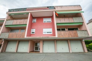 Ein mehrgeschossiges Wohngebäude mit Balkonen, einem zentralen Eingang und Garagen.