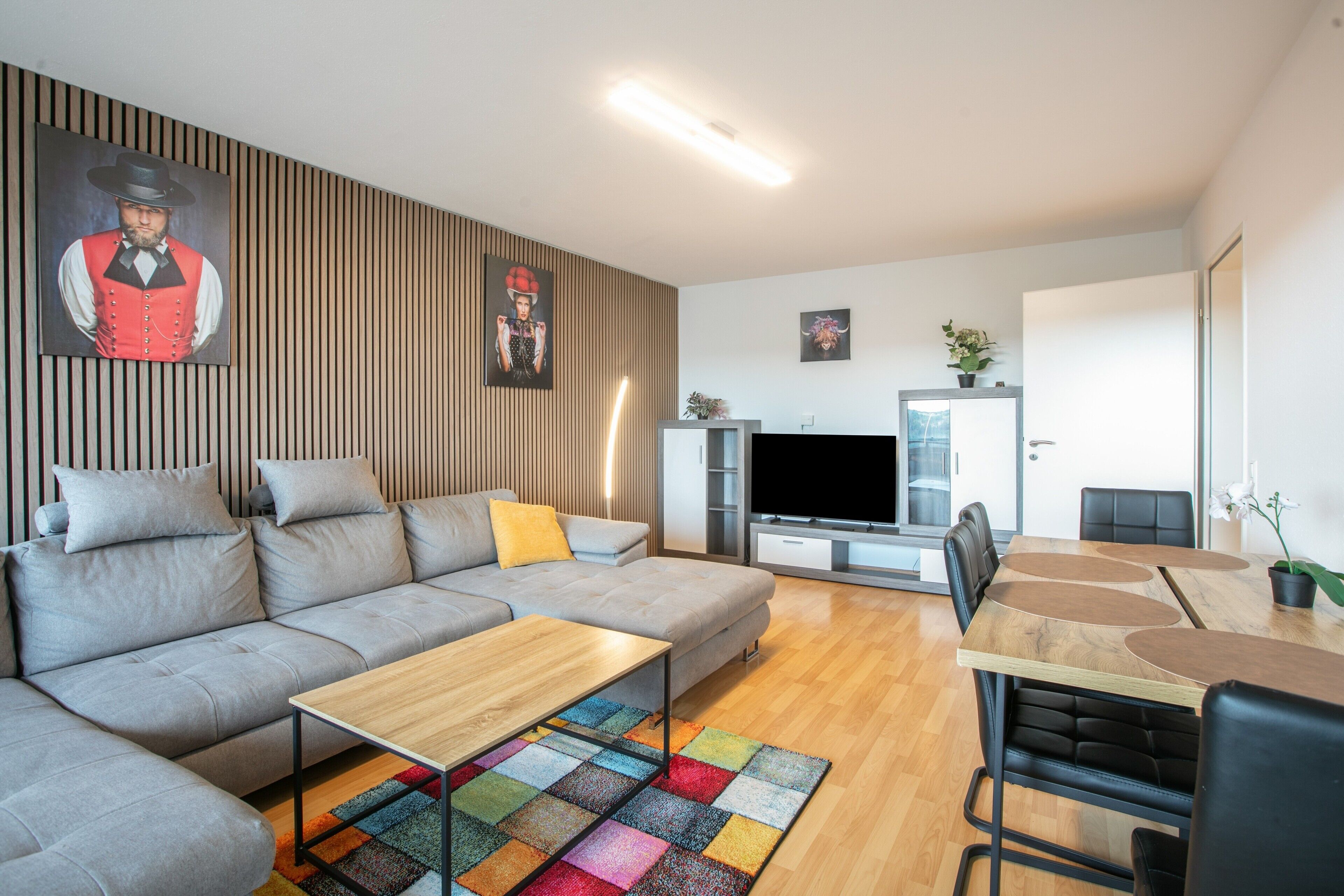 A modern living room with a sectional sofa, a coffee table, a flat-screen TV, and a dining area with a table and chairs.