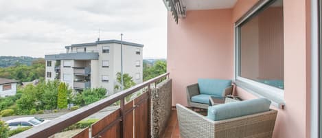 A balcony with wicker furniture, a view of a building, and a wooden fence.