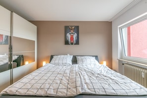 Ein Schlafzimmer mit Bett, Nachttischlampen, einem Bild an der Wand und einem Fenster mit Blick.