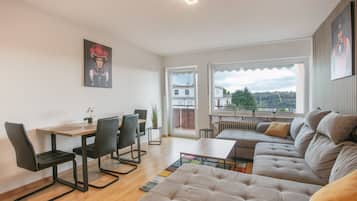 Ein modernes Wohnzimmer mit einer Couch, einem Esstisch, Stühlen und Blick ins Freie.