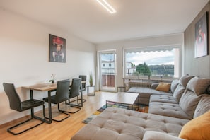 Ein modernes Wohnzimmer mit einer Couch, einem Esstisch, Stühlen und Blick ins Freie.