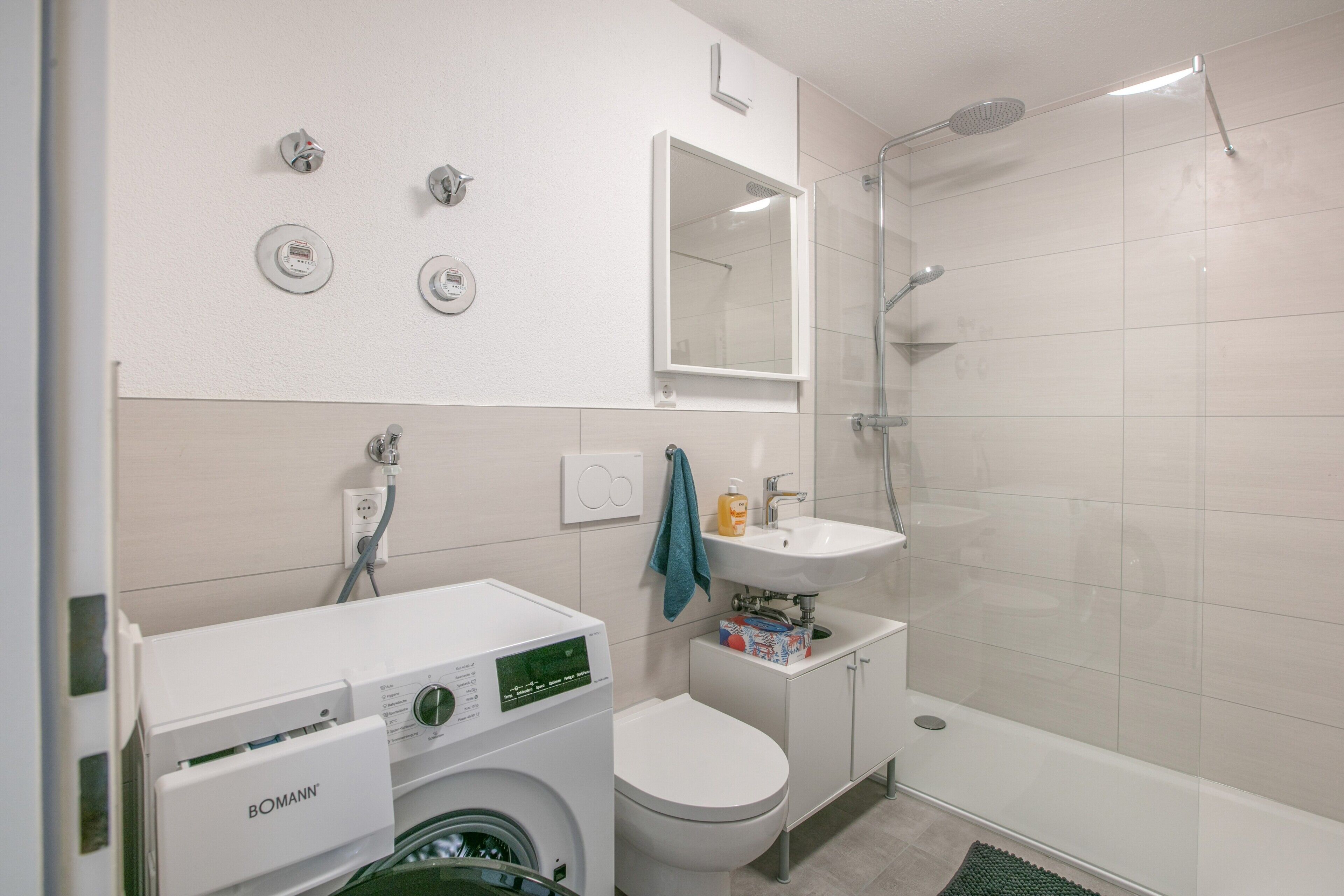 Ein modernes Badezimmer mit Waschmaschine, Toilette, Waschbecken und Dusche.