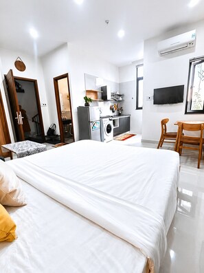 A modern bedroom with a large bed, a built-in washing machine, a TV, and a dining area. - Green Apartment near My Khe Beach and Dragon Bridge - R402 (Đà Nẵng)