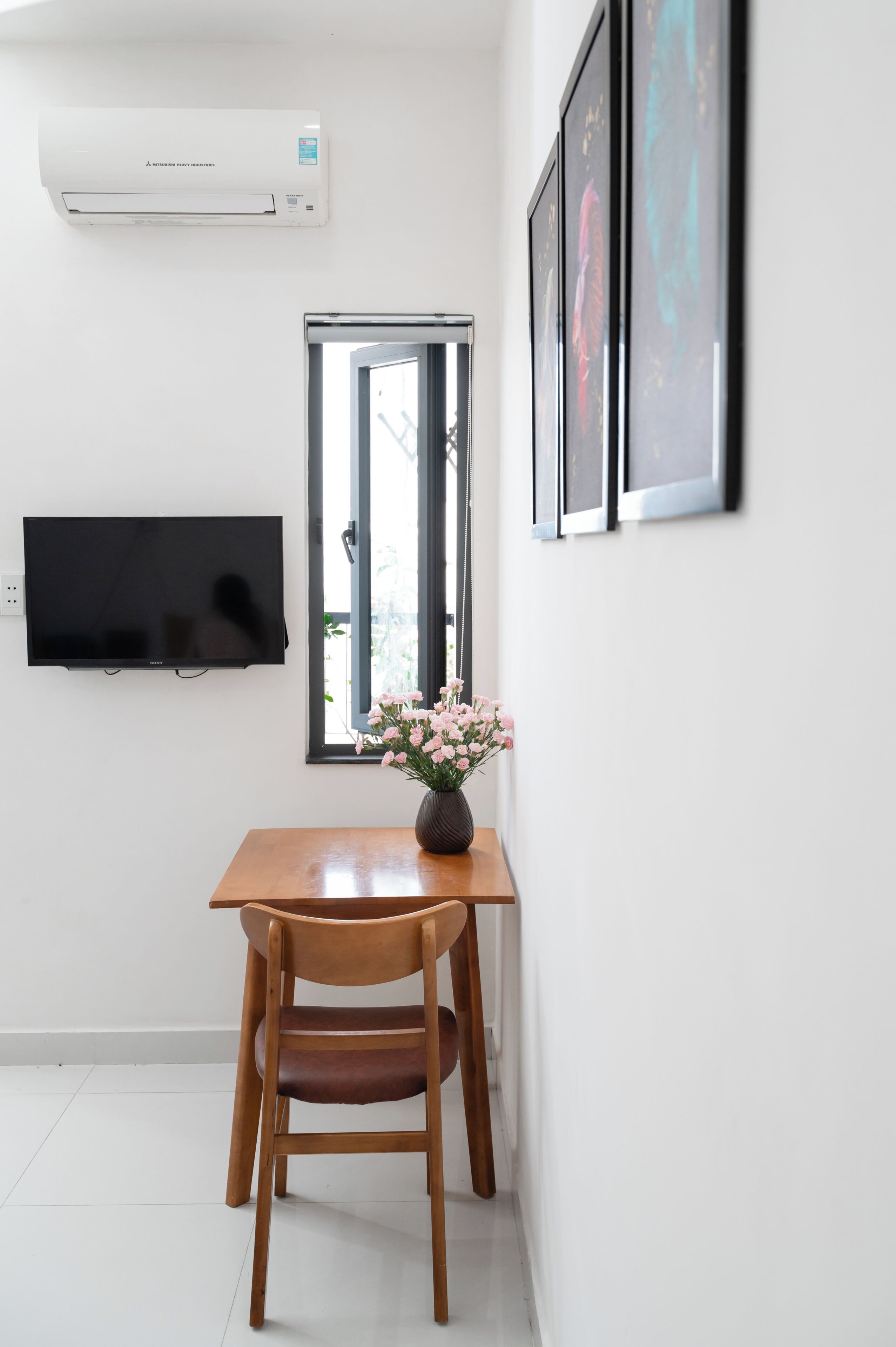 Une pièce comprenant une table en bois, une chaise, un téléviseur à écran plat, une fenêtre et un climatiseur fixé au mur.