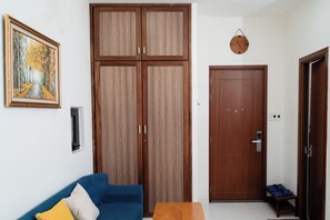 Un salon avec un canapé bleu, une armoire en bois, une porte avec une serrure et une horloge fixée au mur.