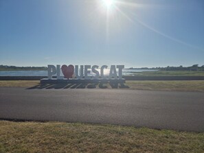 A sign with the text 'PLUESCAT' and a heart symbol, set against a backdrop of a clear sky and a body of water. - Beachfront house renovated in 2025, located on a quiet cul-de-sac 20 meters from the GR34. (Plouescat)