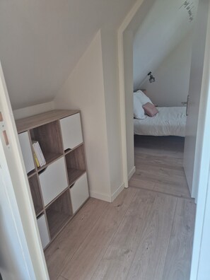 A room with a wooden bookshelf, a bed with white bedding, and a sloped ceiling. - Beachfront house renovated in 2025, located on a quiet cul-de-sac 20 meters from the GR34. (Plouescat)