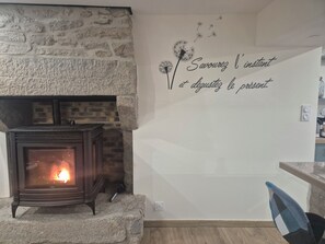 A stone fireplace with a visible fire, a wall with a French phrase, and a modern chair. - Beachfront house renovated in 2025, located on a quiet cul-de-sac 20 meters from the GR34. (Plouescat)