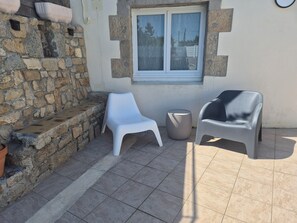 A patio area with stone walls, a window, and two plastic chairs. - Beachfront house renovated in 2025, located on a quiet cul-de-sac 20 meters from the GR34. (Plouescat)