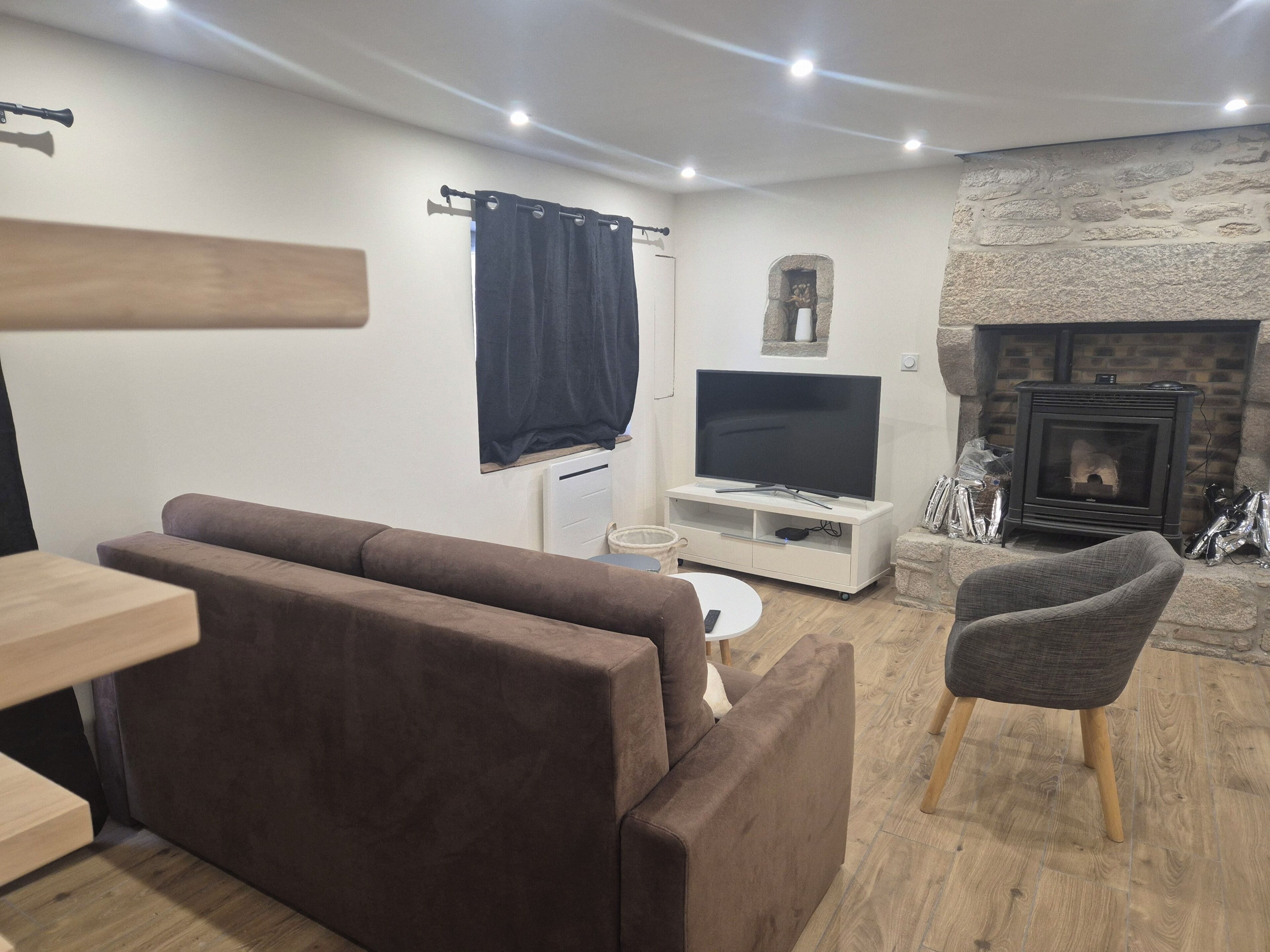 A living room with a sofa, a television on a stand, a stone fireplace, and a small table.