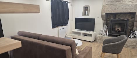 A living room with a sofa, a television on a stand, a stone fireplace, and a small table.