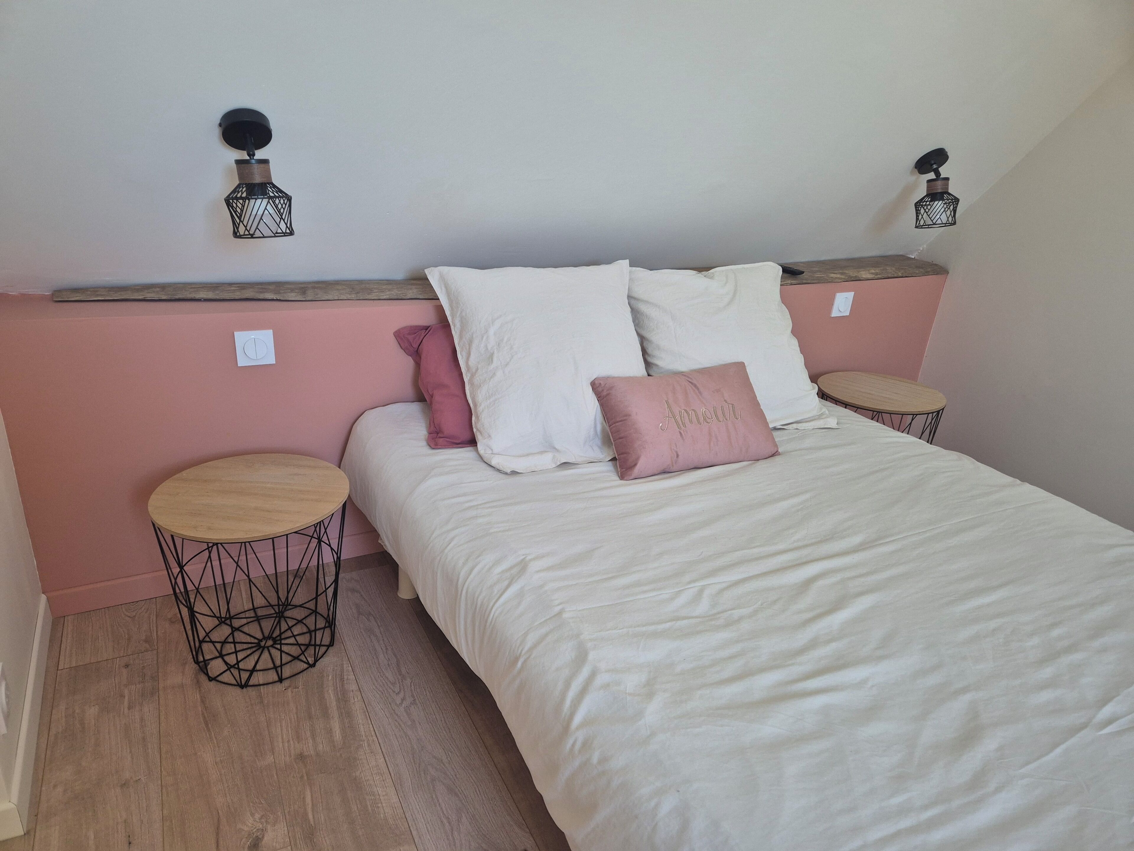 Un dormitorio con una cama, dos mesitas de noche, un aplique en la pared y una pequeña mesa redonda.
