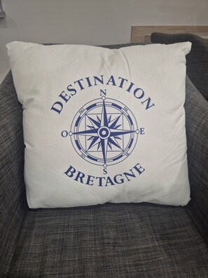 A pillow with a compass and text 'DESTINATION BRETAGNE' on a gray couch. - Beachfront house renovated in 2025, located on a quiet cul-de-sac 20 meters from the GR34. (Plouescat)
