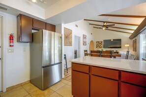 A modern kitchen with a stainless steel refrigerator, wooden cabinets, a ceiling fan, and a dining area with a table and chairs. - The Airman House: Pool/Hot Tub Fun By Lackland AFB (San Antonio)