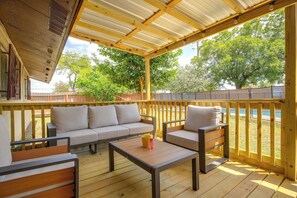 A covered outdoor seating area with a wooden bench and a sofa, a table, and a view of a body of water and trees. - The Airman House: Pool/Hot Tub Fun By Lackland AFB (San Antonio)