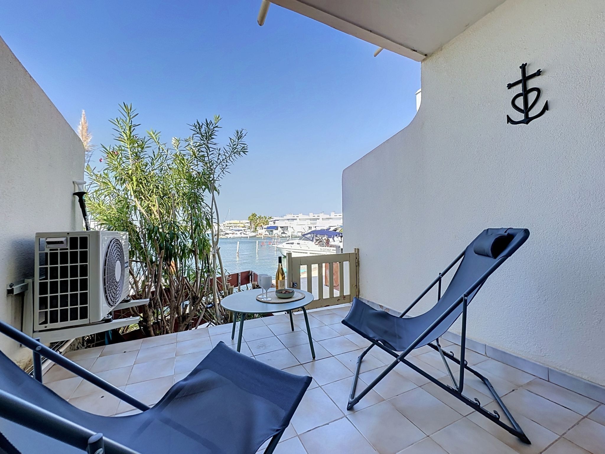 Un balcon avec deux fauteuils, une petite table avec une bouteille et des verres, et une vue sur la mer et les bateaux.