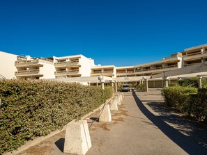 Un immeuble résidentiel à plusieurs étages, doté de balcons, d’une allée pavée et d’une voiture garée.