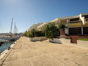 A marina with boats docked, a paved walkway, and modern buildings with balconies. - Ulysse Port de Plage by Interhome (Port Camargue)