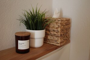 Eine Kerze, ein Topfpflanze und ein gewebter Korb auf einem Regal.