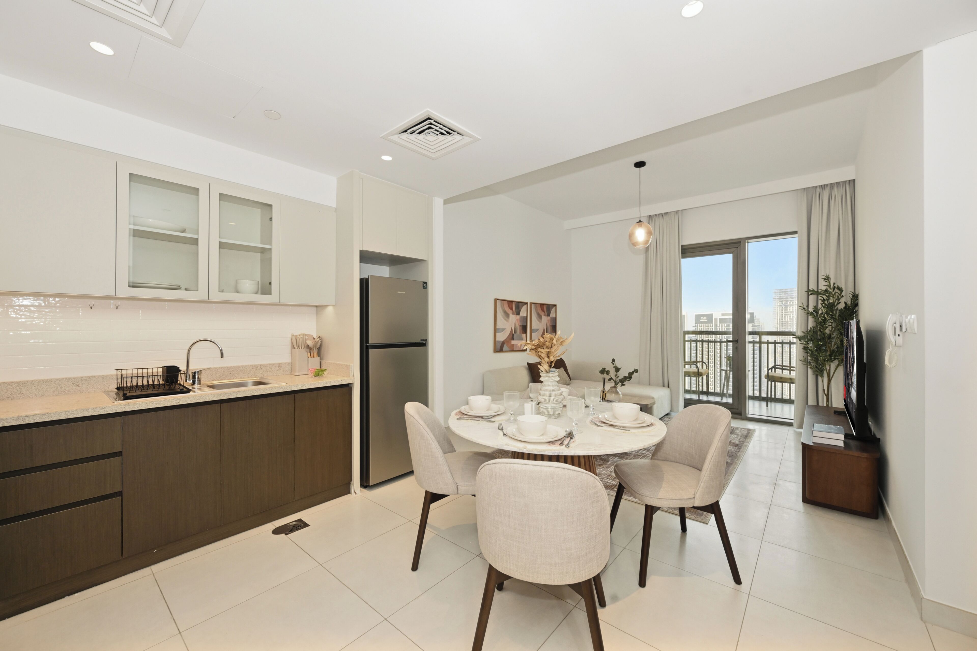 A modern kitchen with a built-in refrigerator, a dining area with a round table and chairs, and a balcony with a view of the city.