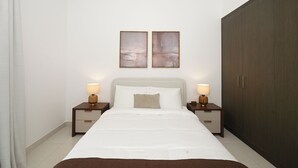 Quarto com cama, duas mesas de cabeceira com luminárias, um guarda-roupa e duas pinturas penduradas na parede.