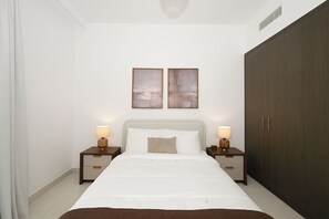 A bedroom with a bed, two bedside tables with lamps, a wardrobe, and two wall-mounted paintings. - Bloomfields 1BR in Creekside 18 (Dubai)